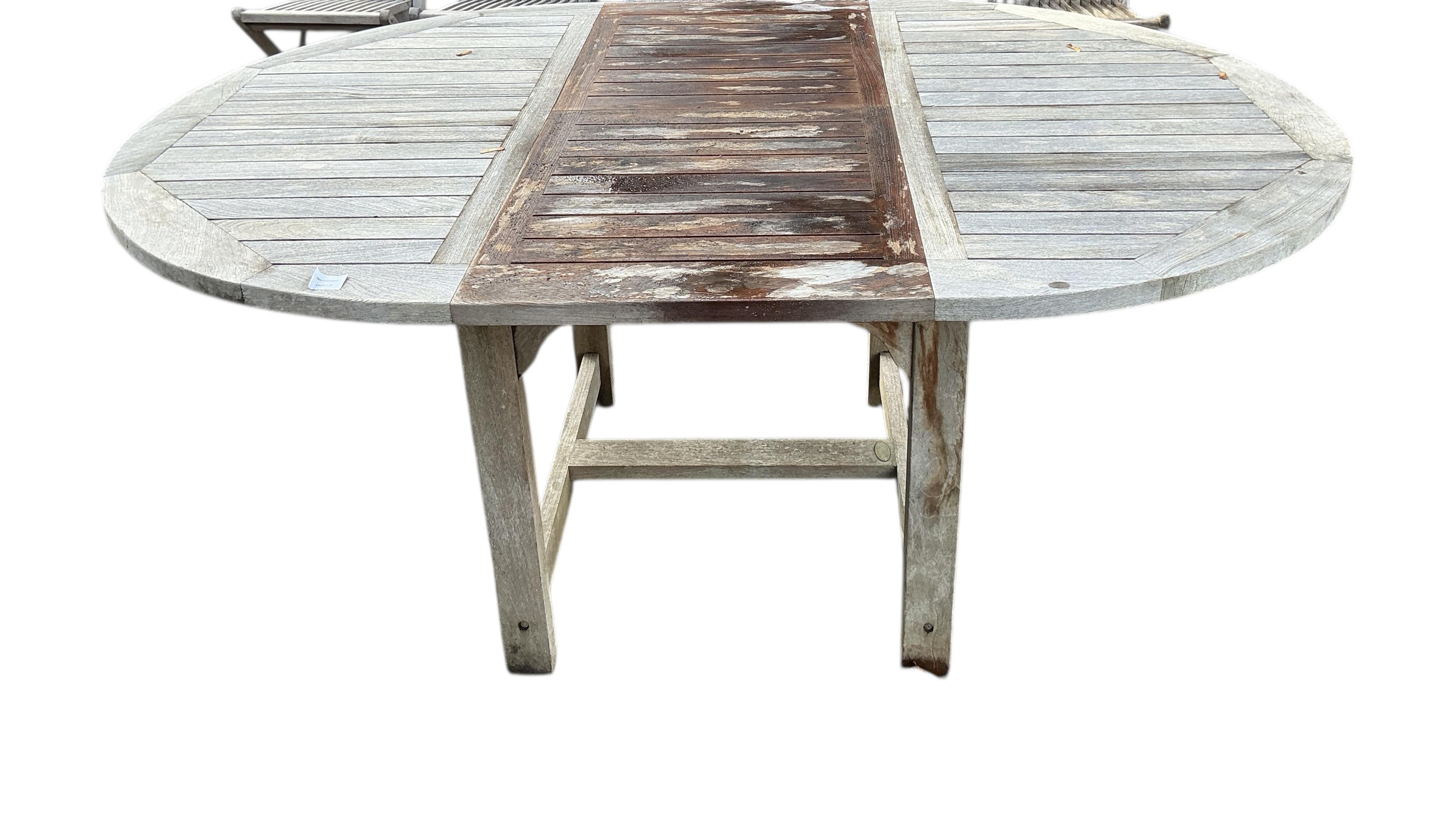 A Laidlays teak oval extending garden table, width 169cm extended, depth 120cm, height 75cm together with eight folding weathered teak garden chairs